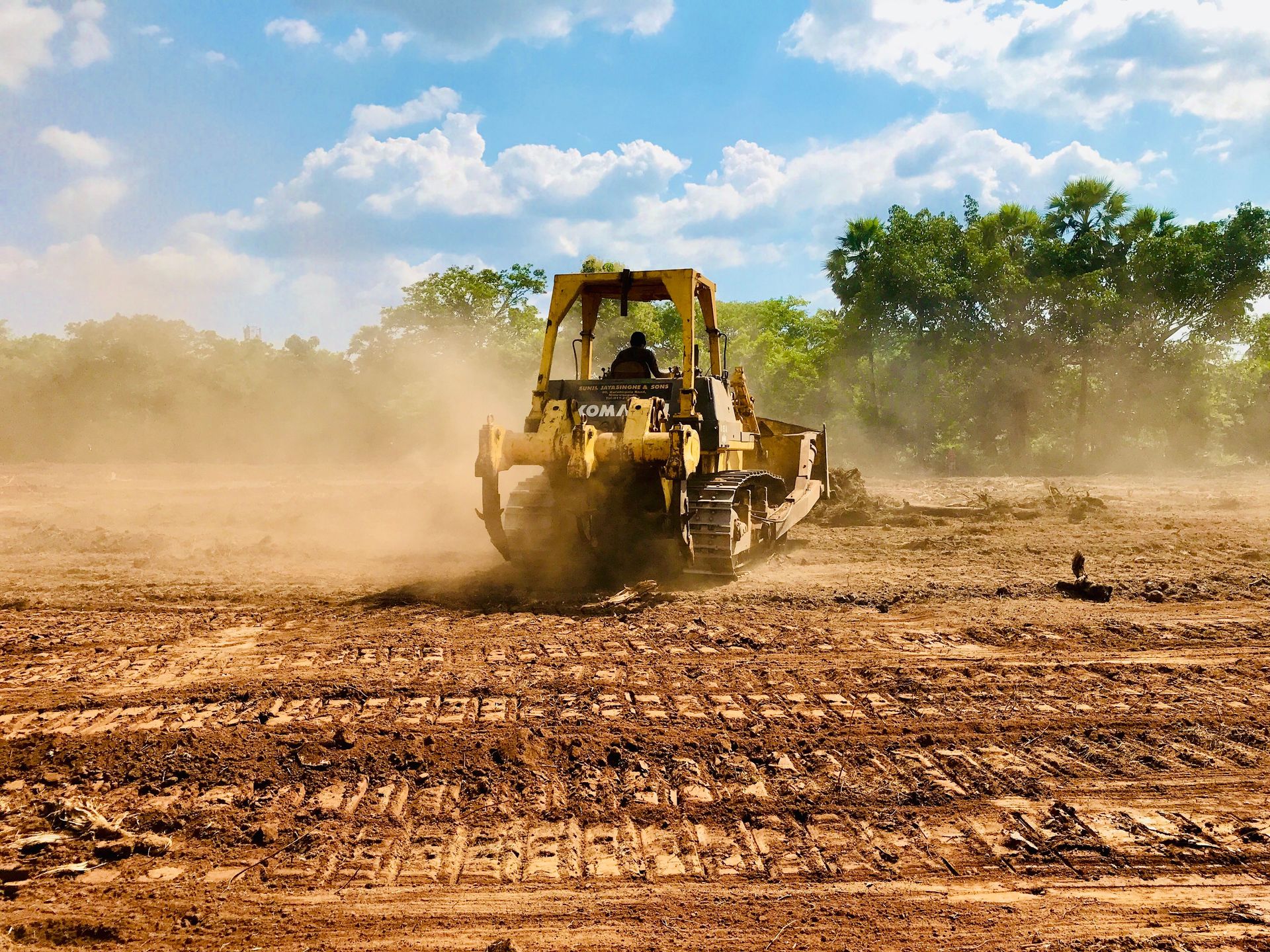 A yellow bulldozer working on a dusty construction site, moving earth under a clear sky.